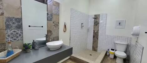Une salle de bain moderne avec un grand miroir, un lavabo blanc, une zone douche et des toilettes.