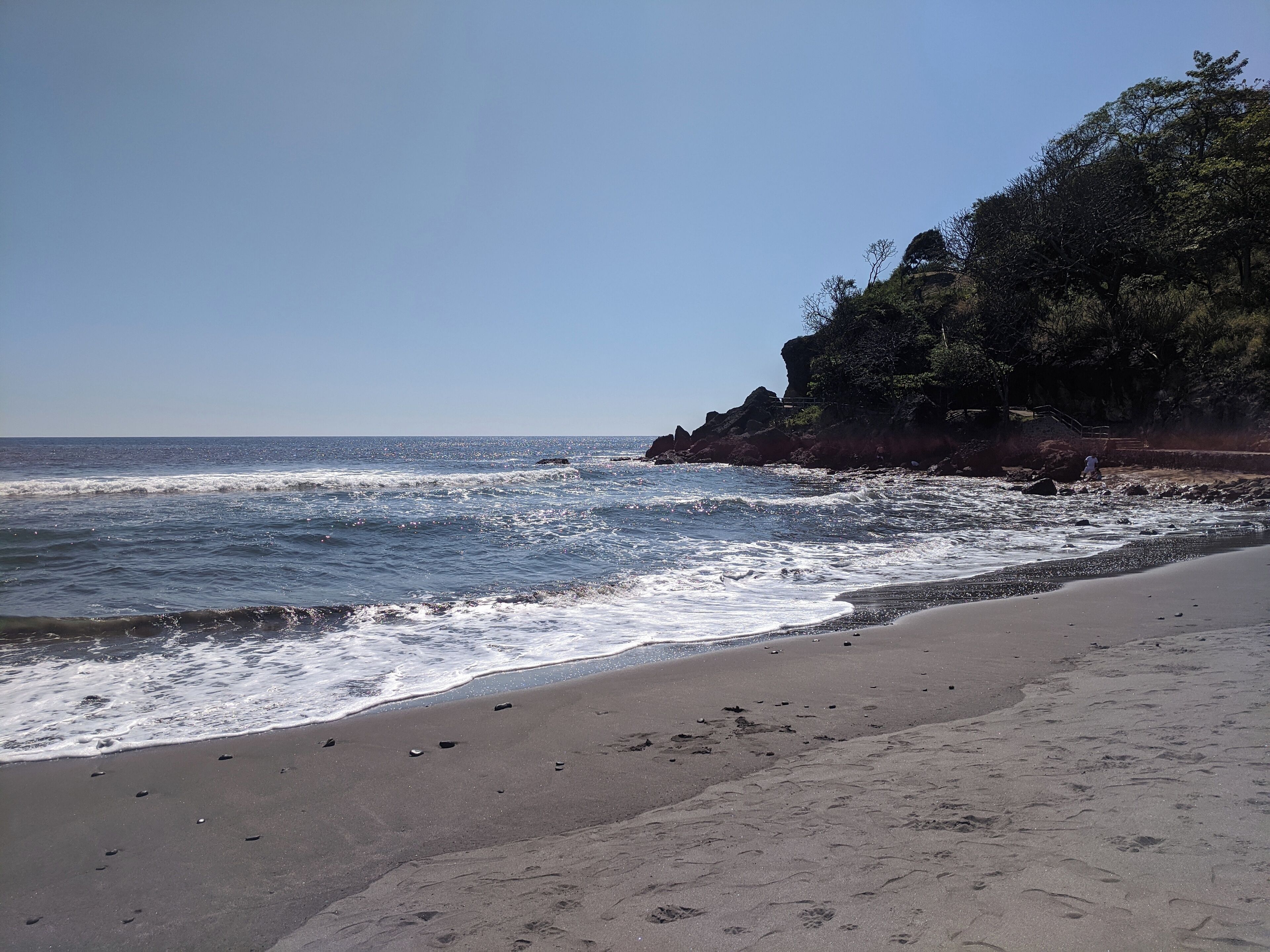 Ein Strand mit Wellen, einer felsigen Klippe und einem klaren Himmel.