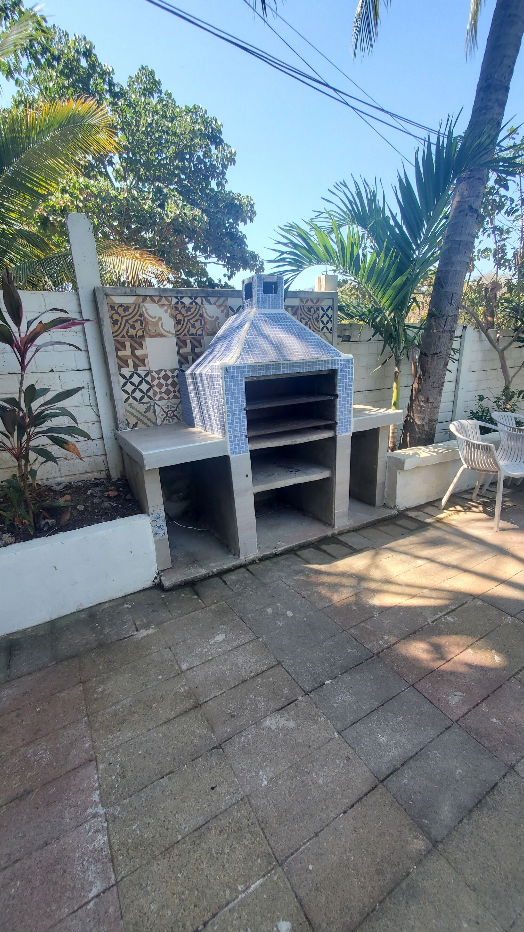 An outdoor barbecue area with a tiled chimney, surrounded by potted plants and a white wall.