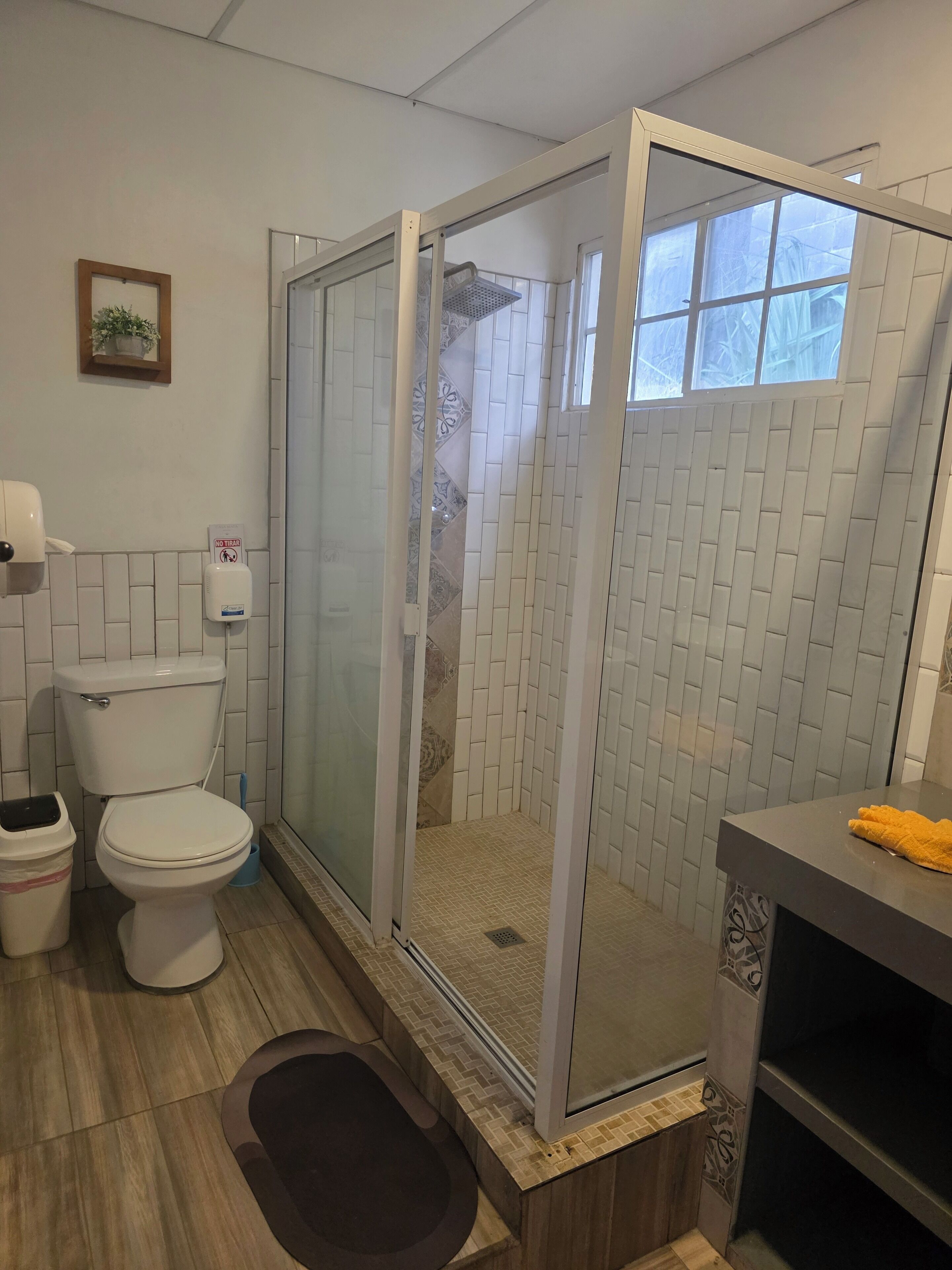 A bathroom with a toilet, a glass-enclosed shower, a sink, and a trash bin.