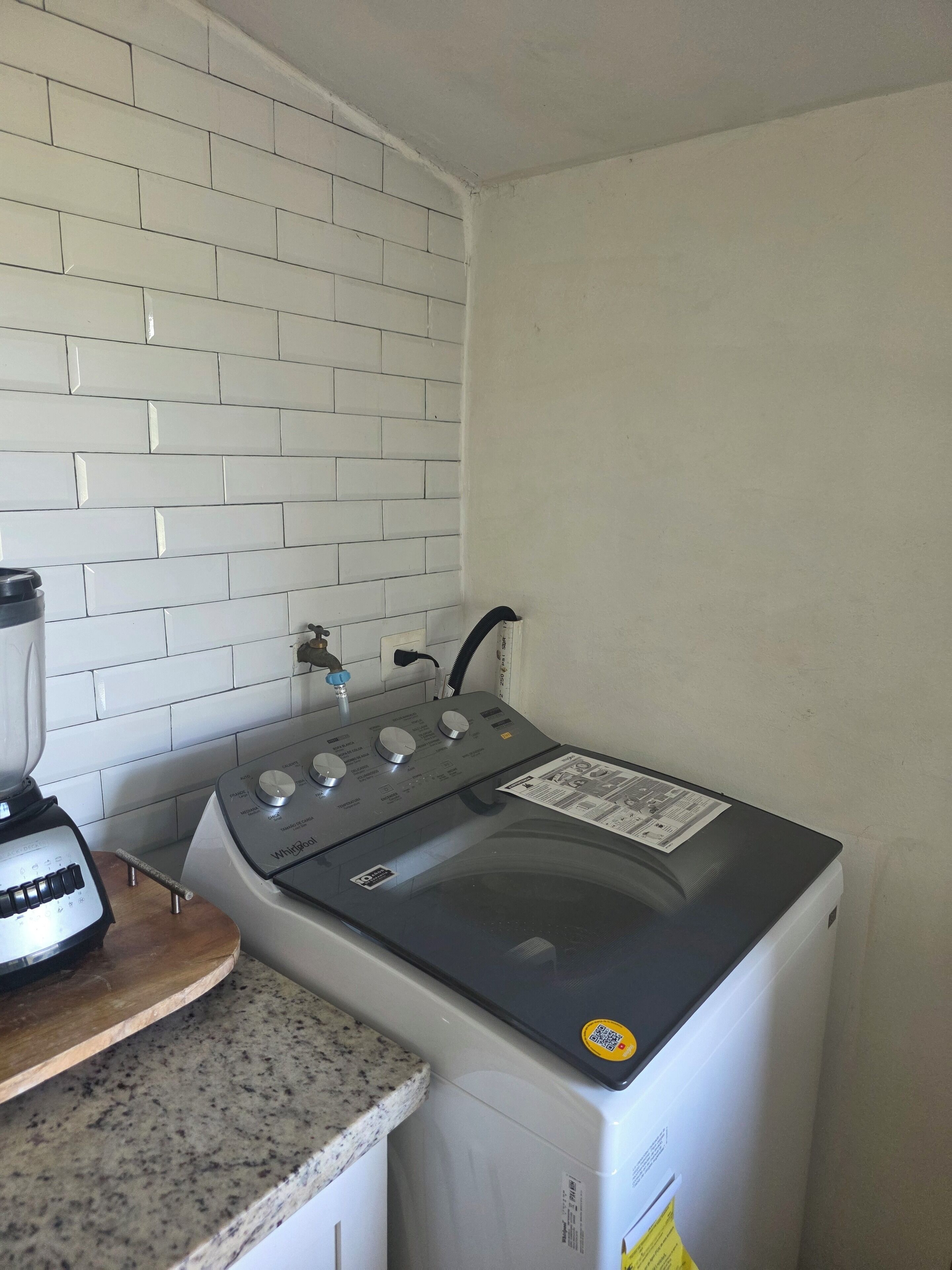 Une cuisine compacte avec un dosseret de carrelage blanc, une cuisinière encastrée, un plan de travail avec un mixeur et un petit évier.