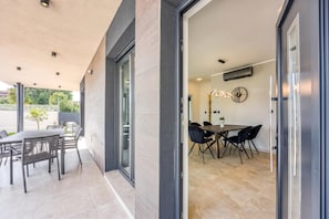 A modern outdoor dining area with a table and chairs, a covered patio, and a view of the interior dining space. - Villa Gigi With Private Pool (Visnjan)