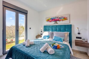 A bedroom with a large bed, a view through a sliding door, a painting on the wall, and a bedside table with a lamp. - Villa Gigi With Private Pool (Visnjan)