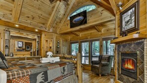 A log cabin interior with a large bed, a fireplace, a television, and a view of the outdoors. - Mountain Pooladise | Blue Ridge, Ga (Epworth)