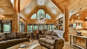 A log cabin interior with a wooden ceiling, a fireplace, a dining area, and a cozy seating arrangement. - Mountain Pooladise | Blue Ridge, Ga (Epworth)
