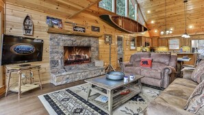 Ein Blockhaus-Interieur mit Kamin aus Stein, Holzwänden, einem Fernseher und einer gemütlichen Sitzecke.