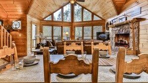 Ein Interieur einer Holzhütte mit Esstisch, Stühlen, Kamin und Fernseher.
