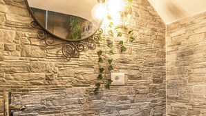 A bathroom with a stone sink, a white pedestal sink, a mirror, and a wall-mounted light fixture. - Notti Magiche (Santa Maria di Castellabate)