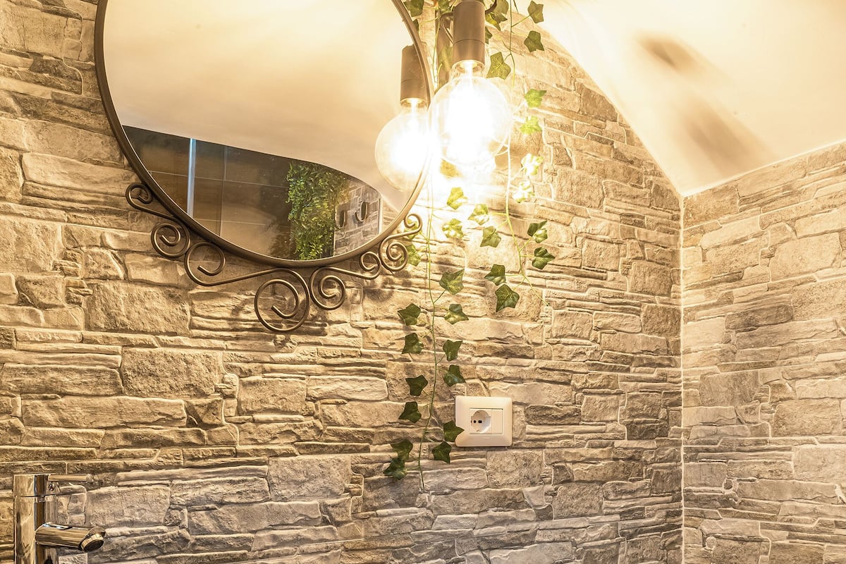 Une salle de bain avec un lavabo en pierre, un lavabo sur colonne blanc, un miroir et un luminaire fixé au mur.