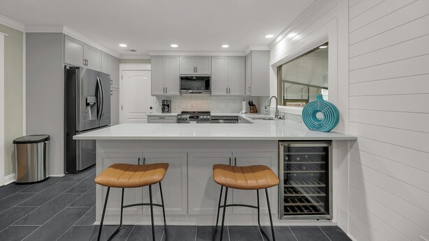A modern kitchen with white cabinetry, a stainless steel refrigerator, a built-in oven, and a wine cooler. There are two bar stools and a window with a view. - 3 Mi to Beach, Waterfront Charleston Home w/ Patio (Charleston)