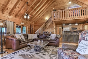 A wooden cabin interior with a living room, kitchen, and a staircase. - Above It All | Ellijay, GA (Ellijay)