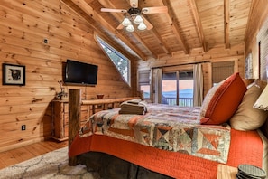 A wooden cabin bedroom with a bed, a TV, a window, and a ceiling fan. - Above It All | Ellijay, GA (Ellijay)