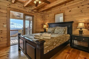 A wooden cabin bedroom with a large bed, two bedside tables, a ceiling fan, and a view through a sliding door.
