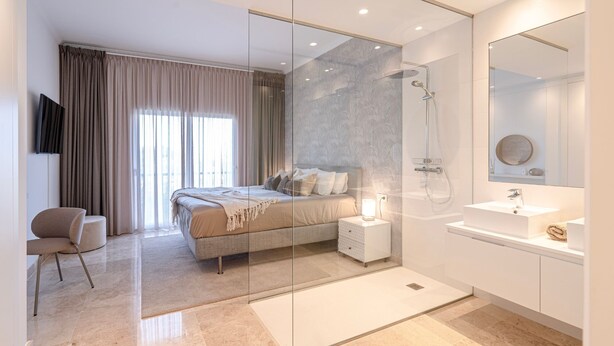 A modern bedroom with a bed, bedside table, and a glass-enclosed shower.