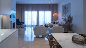 A modern living room with a sofa set, a dining table, and a TV mounted on the wall.