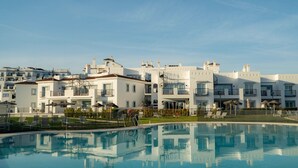 A modern hotel with a swimming pool, multiple balconies, and a clear view of the surrounding area.