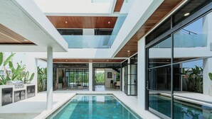 A modern indoor pool area with glass walls, a wooden ceiling, and a grill outside. - Luxurious 4 Bedroom villa with swimming pool in Uluwatu (Uluwatu)