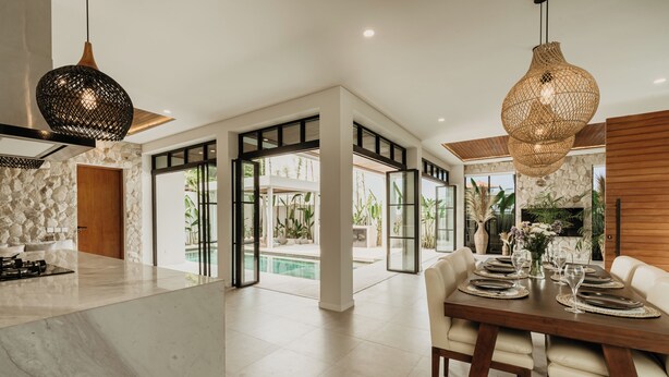 A spacious kitchen with a marble countertop, a dining area with a wooden table set for four, and a view of an outdoor pool area. - Luxurious 4 Bedroom villa with swimming pool in Uluwatu (Uluwatu)