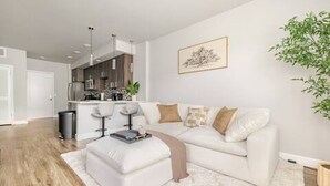 A modern living room with a white sofa, a coffee table, and a small side table. There is a kitchen area in the background with a dining table and chairs. - Mid-rise Modern Lux loft In The City (Sacramento)