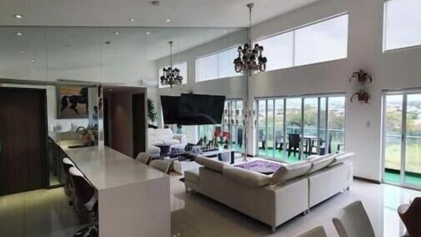 A modern kitchen with a central island, a dining area with white chairs, and large windows offering a view of the outdoors. - Penthouse safe and beautiful, with stunning views (San José)