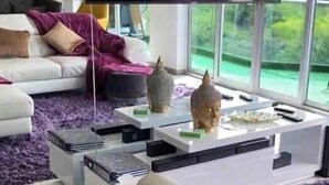 A modern living room with a large flat-screen TV mounted on the wall, a white sofa, a coffee table with decorative items, and a view of greenery outside. - Penthouse safe and beautiful, with stunning views (San José)