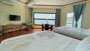 Habitación de hotel con dos camas, un escritorio, televisión y vista al mar.