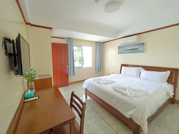 A hotel room with a bed, a desk, a chair, a TV, a window with curtains, and a painting on the wall.