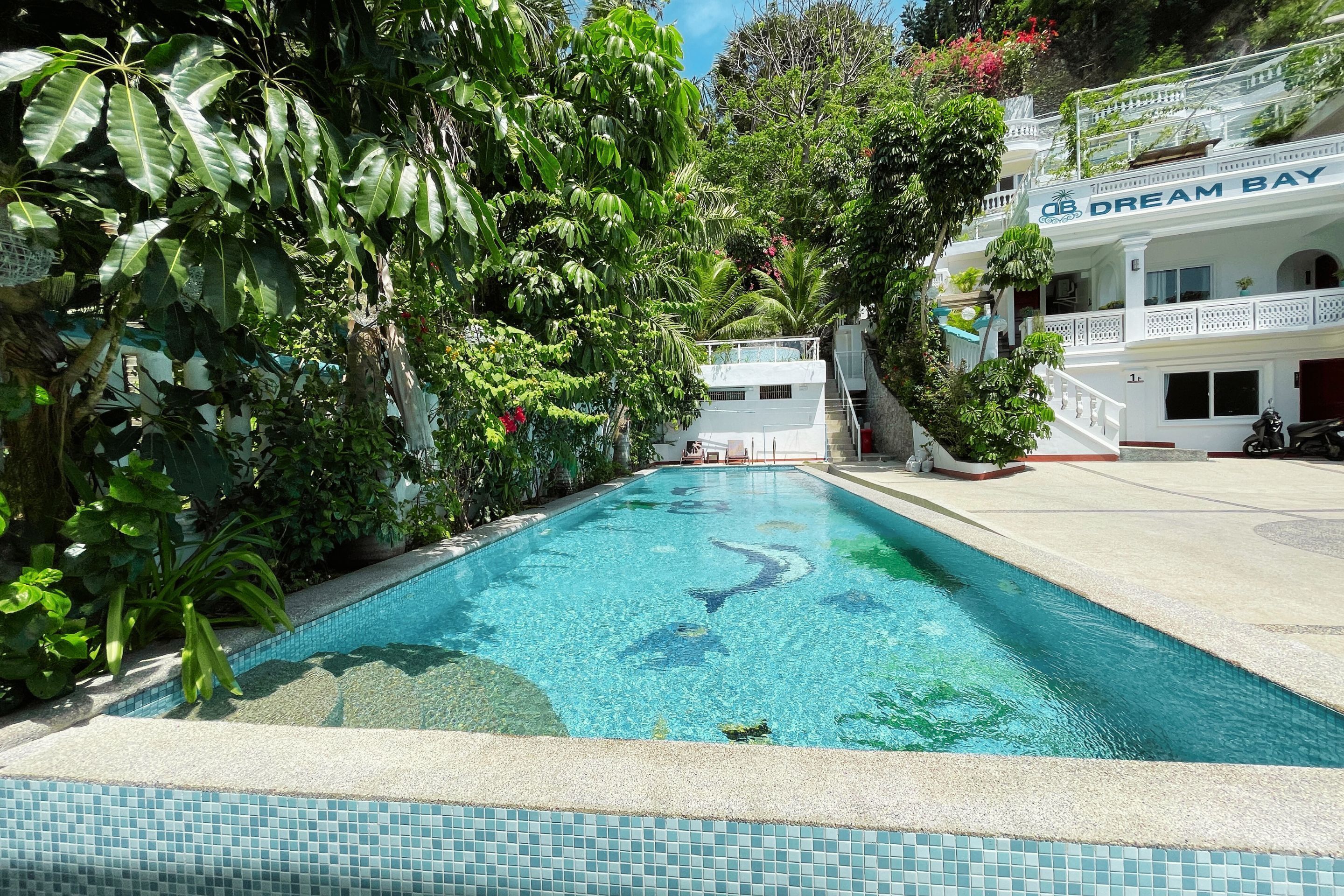 A swimming pool surrounded by lush greenery, with a building labeled "Dream Bay" in the background.