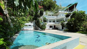Una piscina rodeada de exuberante vegetación, con un edificio de varios pisos que cuenta con balcones y un letrero que dice "DREAM BAY RESORT".