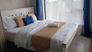 Una cama bien tendida con ropa de cama blanca y marrón, un cabecero de madera y cortinas azules.