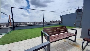 Terraza en la azotea con un banco de madera, césped artificial y barandilla de metal.