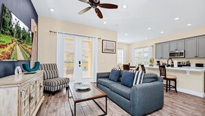 A modern living room with a sofa, coffee table, and striped armchair. There is a kitchen area with cabinets and appliances.
