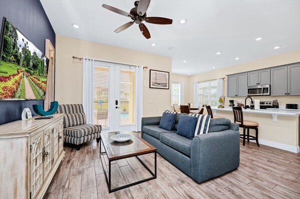 A modern living room with a sofa, coffee table, and striped armchair. There is a kitchen area with cabinets and appliances.