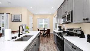 A modern kitchen with a central island, stainless steel appliances, and a dining area with a table and chairs. - Waterfront Cottage | Private Pool + Margaritaville & Waterpark Access - 3008PH (Kissimmee)