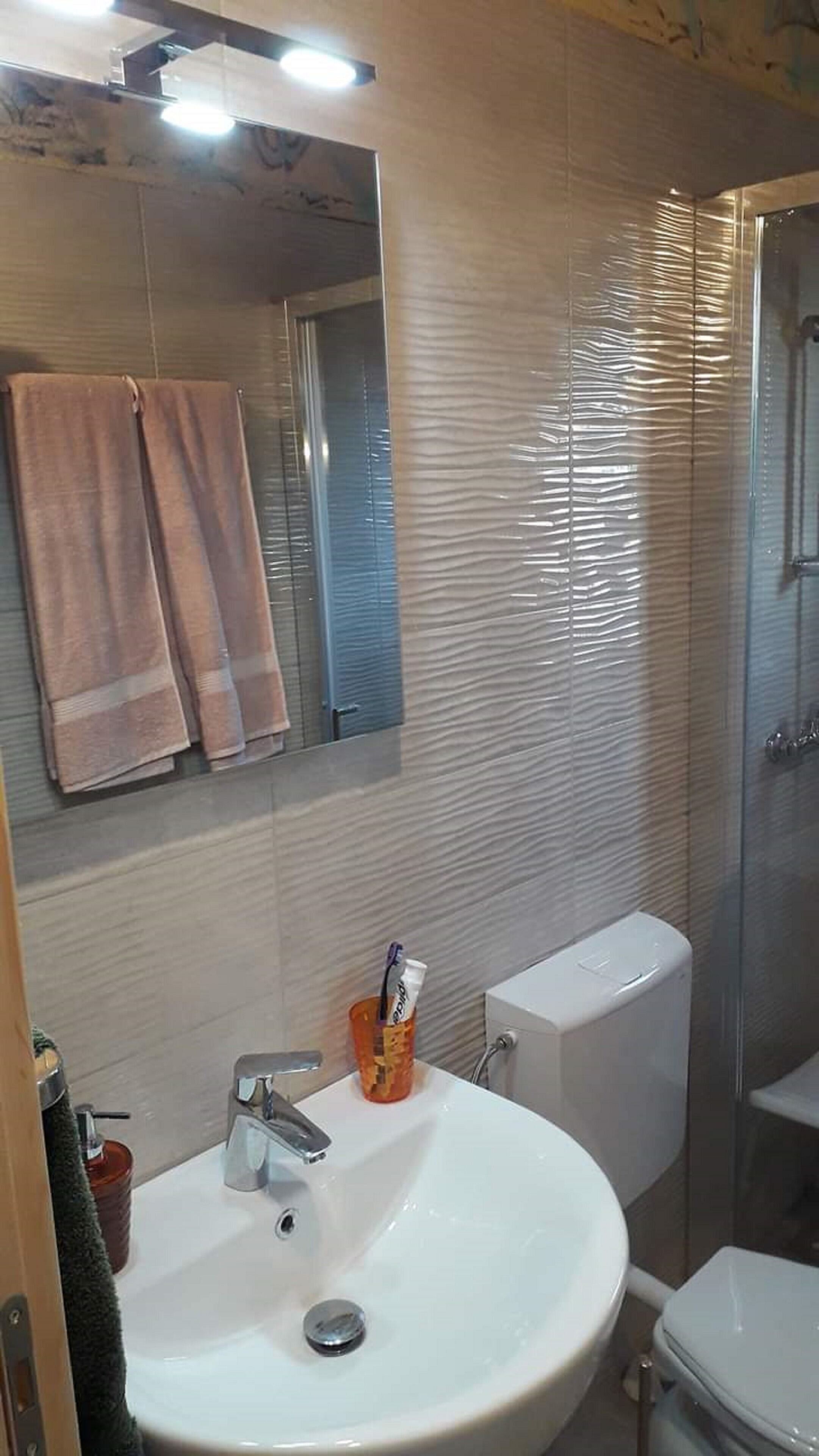 Een badkamer met een wit wastafel, een spiegel en een toilet. Handdoeken hangen aan de muur.