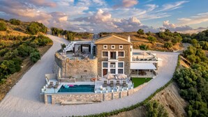 A stone villa with a swimming pool, outdoor seating, and a view of the surrounding landscape. - Saronic Citadel Luxury Villa | Private Estate on Salamina Island (Perani)