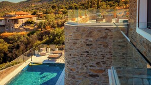 A stone building with a glass balcony overlooking a pool and a mountainous landscape. - Saronic Citadel Luxury Villa | Private Estate on Salamina Island (Perani)