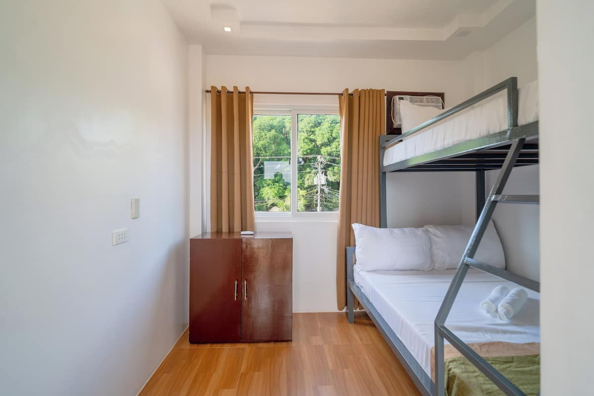 Una habitación pequeña y limpia con una cama litera, un armario de madera y una ventana con cortinas.