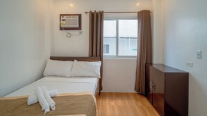 A hotel room with a bed, a wooden cabinet, a window with curtains, and an air conditioning unit on the wall. - Upgrace Inn Coron (Coron)