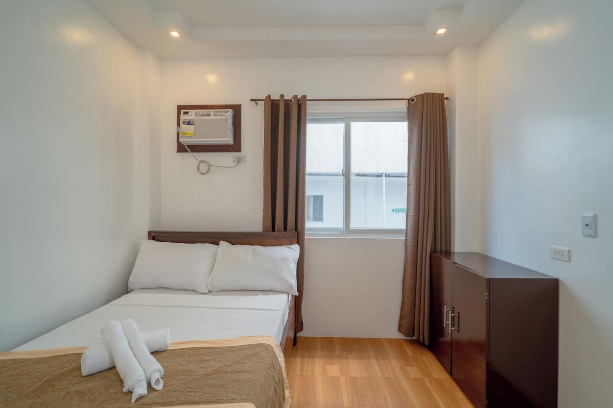 Una habitación de hotel con una cama, un armario de madera, un ventanal con cortinas y un equipo de aire acondicionado en la pared.
