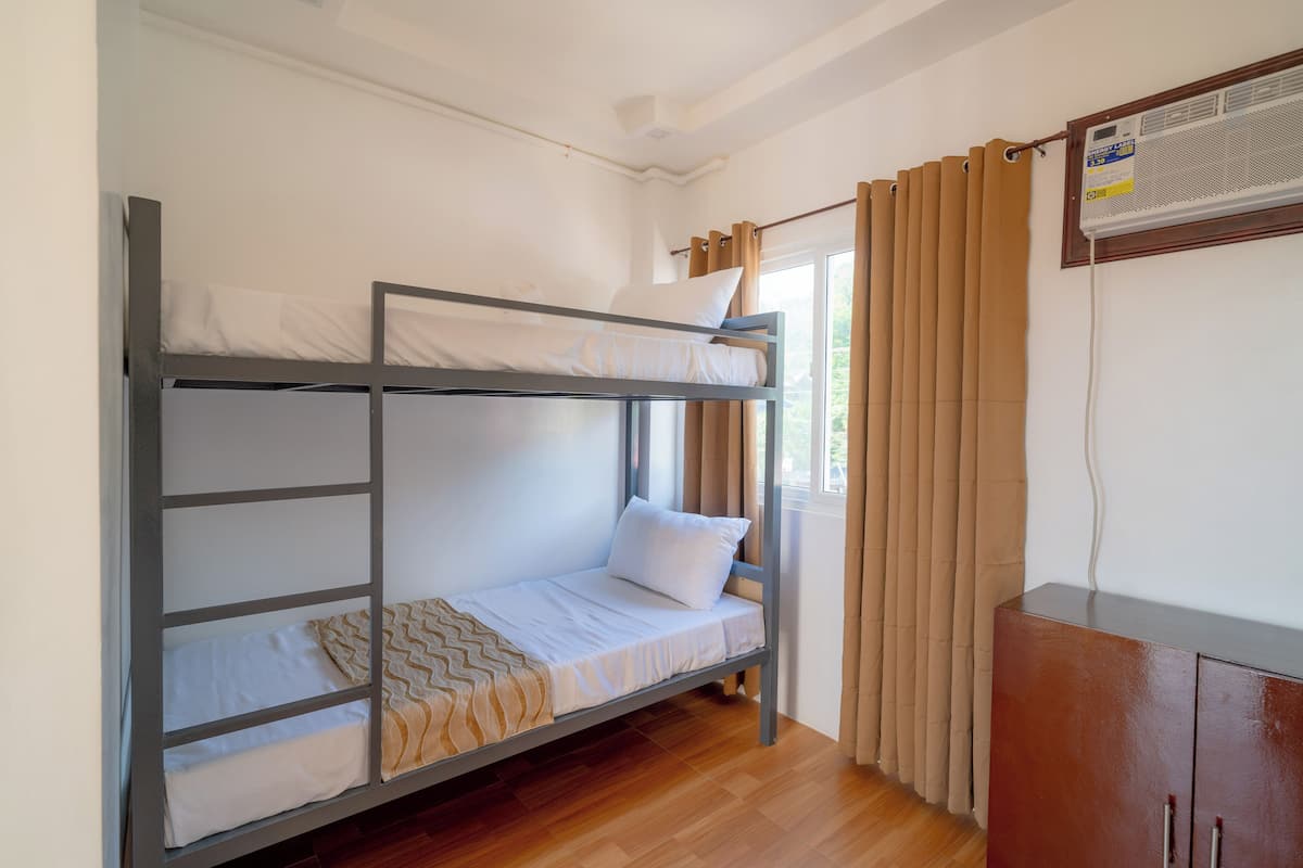 Habitación con literas, suelo de madera, ventana con cortinas y un armario.