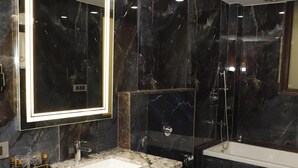 Un baño moderno con tocador de mármol, un espejo grande con marco iluminado, una bañera y una ducha.