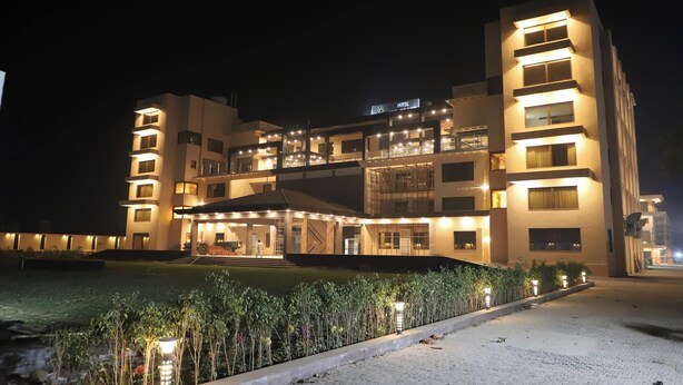 Un hotel de varios pisos con una entrada bien iluminada y un jardín ajardinado.