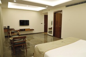 Quarto de hotel com cama, televisão, escrivaninha e espelho.