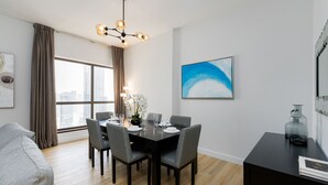 Un espace repas moderne avec une table noire dressée pour quatre personnes, des chaises grises et un lustre.