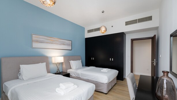 Une chambre d’hôtel avec deux lits, un bureau, une chaise, un grand vase et un tableau au mur.