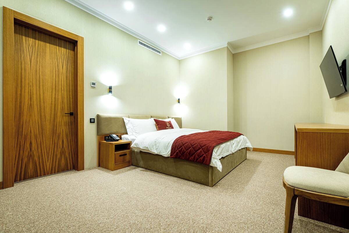 A bedroom with a bed, bedside tables, a chair, a TV, and a door.