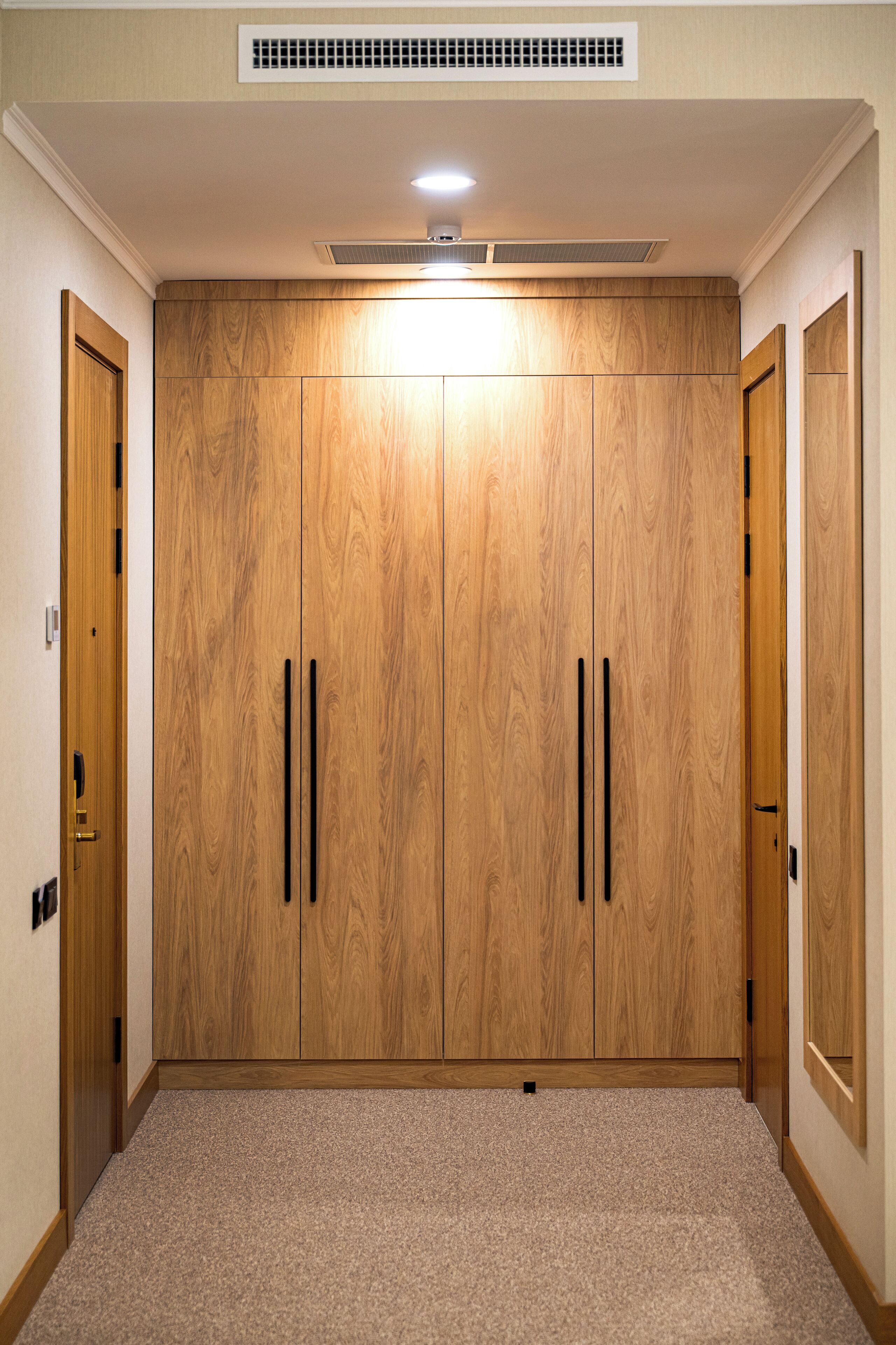 Een kamer met een grote houten garderobe, een vloerbedekking en een ventilatieopening in het plafond.
