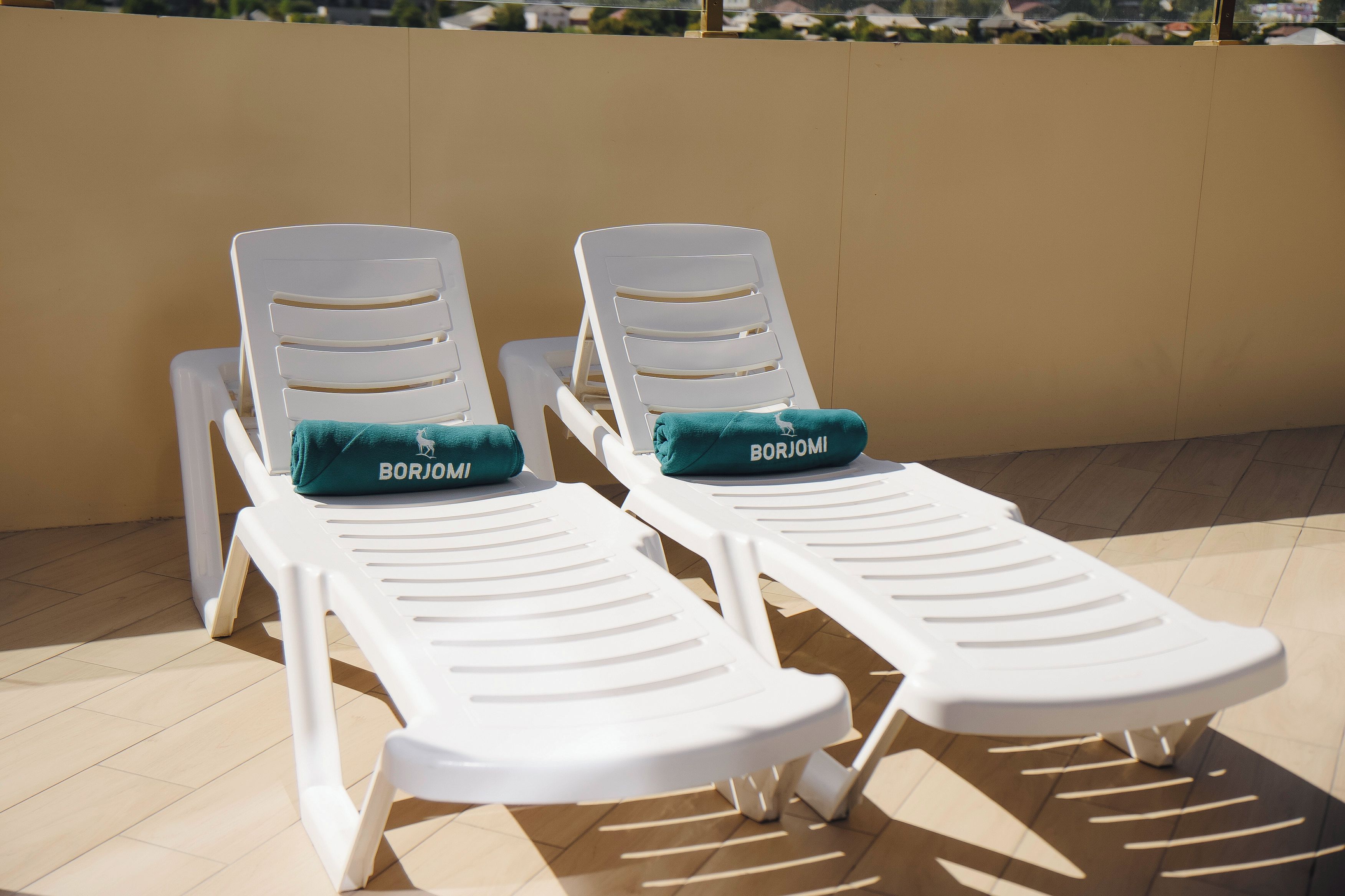 Deux fauteuils blancs avec des coussins verts, portant l’inscription « BORJOMI », sont placés sur un sol carrelé, devant un mur de couleur beige.
