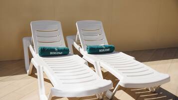 Deux fauteuils blancs avec des coussins verts, portant l’inscription « BORJOMI », sont placés sur un sol carrelé, devant un mur de couleur beige.